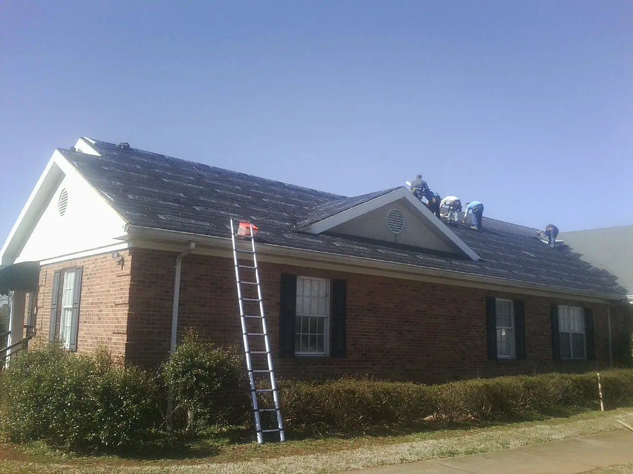 Crew tearing shingles off a brick ranch roof with a ladder set — Metal Roof Repair work by our crew in Scenery Hill