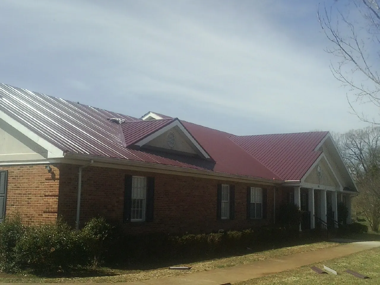 Red metal roof with gabled entries on a long brick building, from a Hail Damage Roof Repair job in Scenery Hill