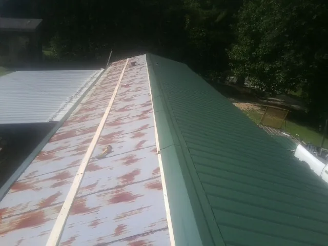 Old rusted panels beside newly installed green metal roofing — Wind Damage Roof Repair by Roofing Brothers in Scenery Hill