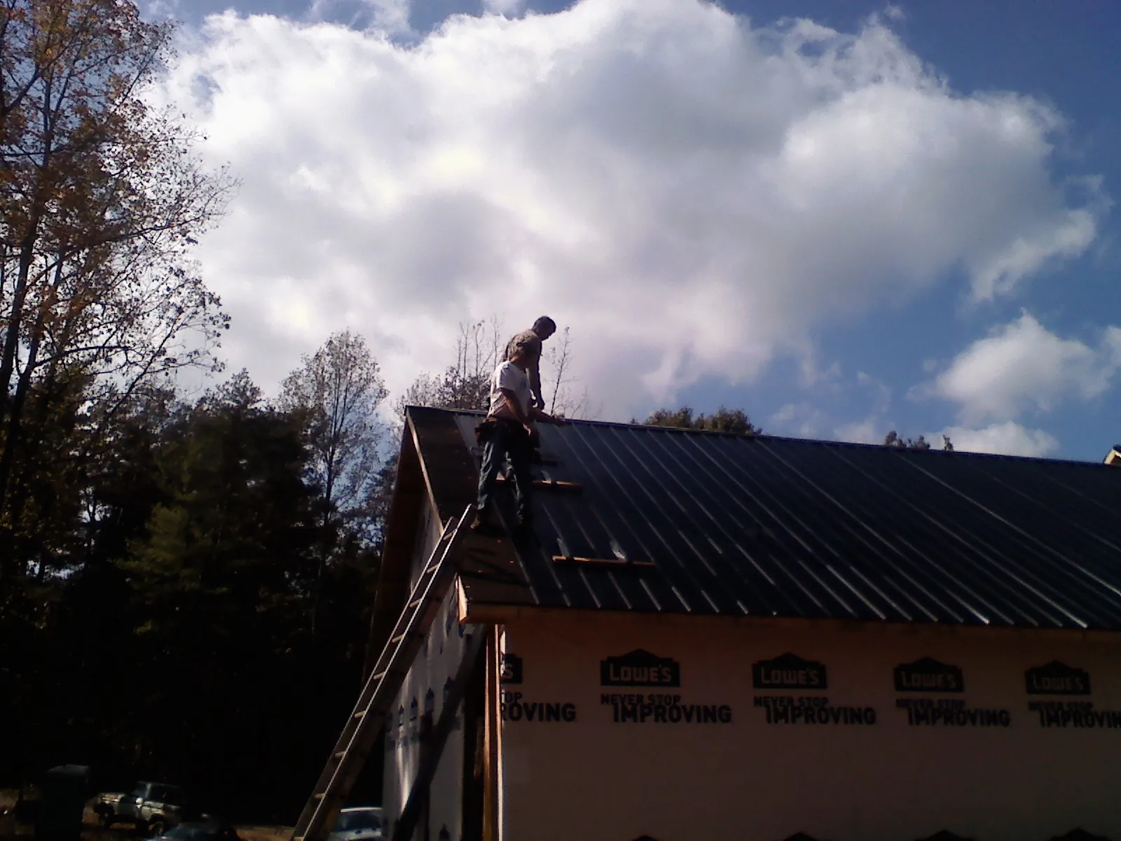 Roofer fastening dark metal panels high against a cloudy sky, from a Roof Inspection job in Scenery Hill