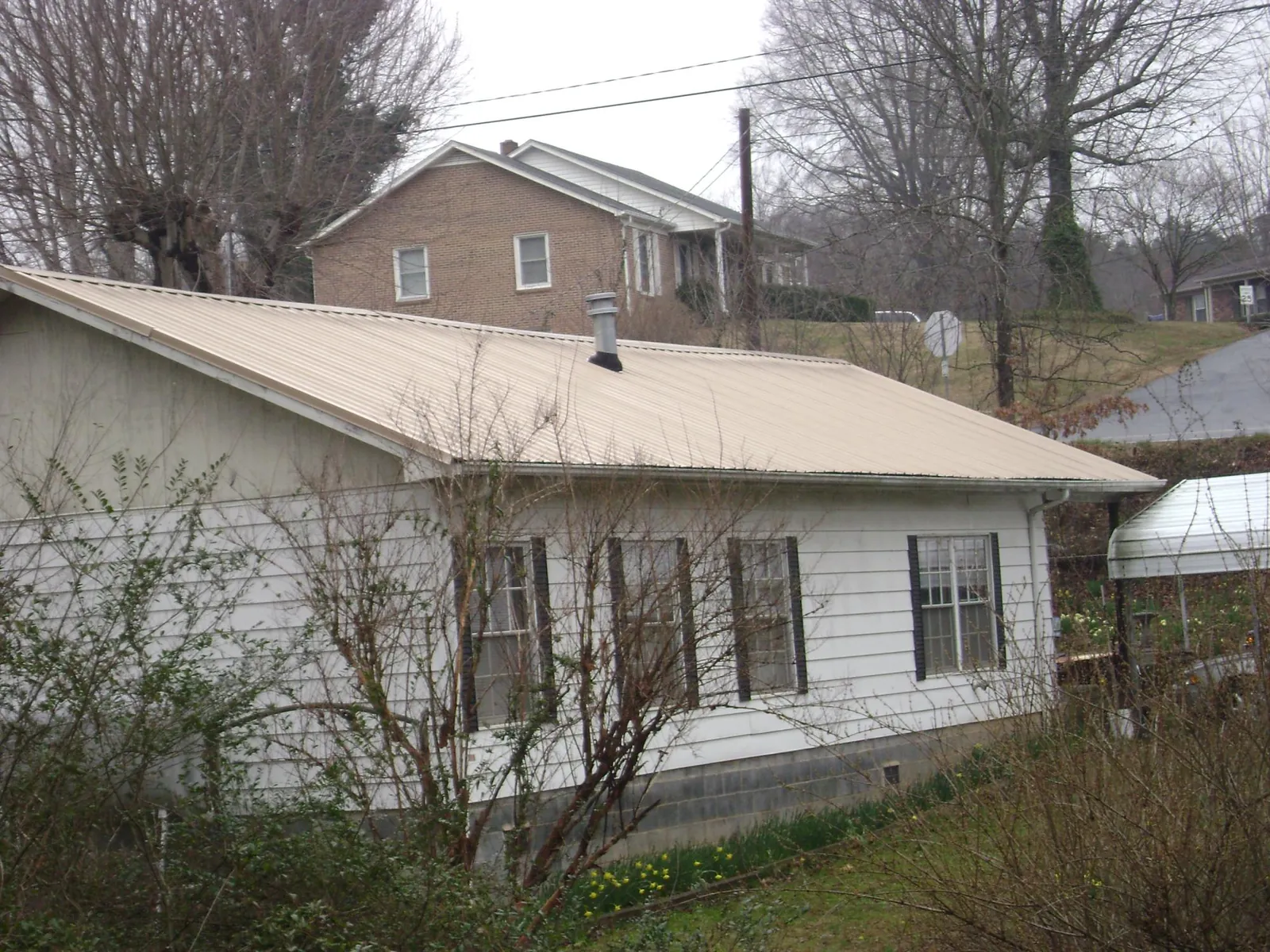 Tan metal roof on a white sided house set into a hillside — Commercial Roofing by Roofing Brothers in Scenery Hill
