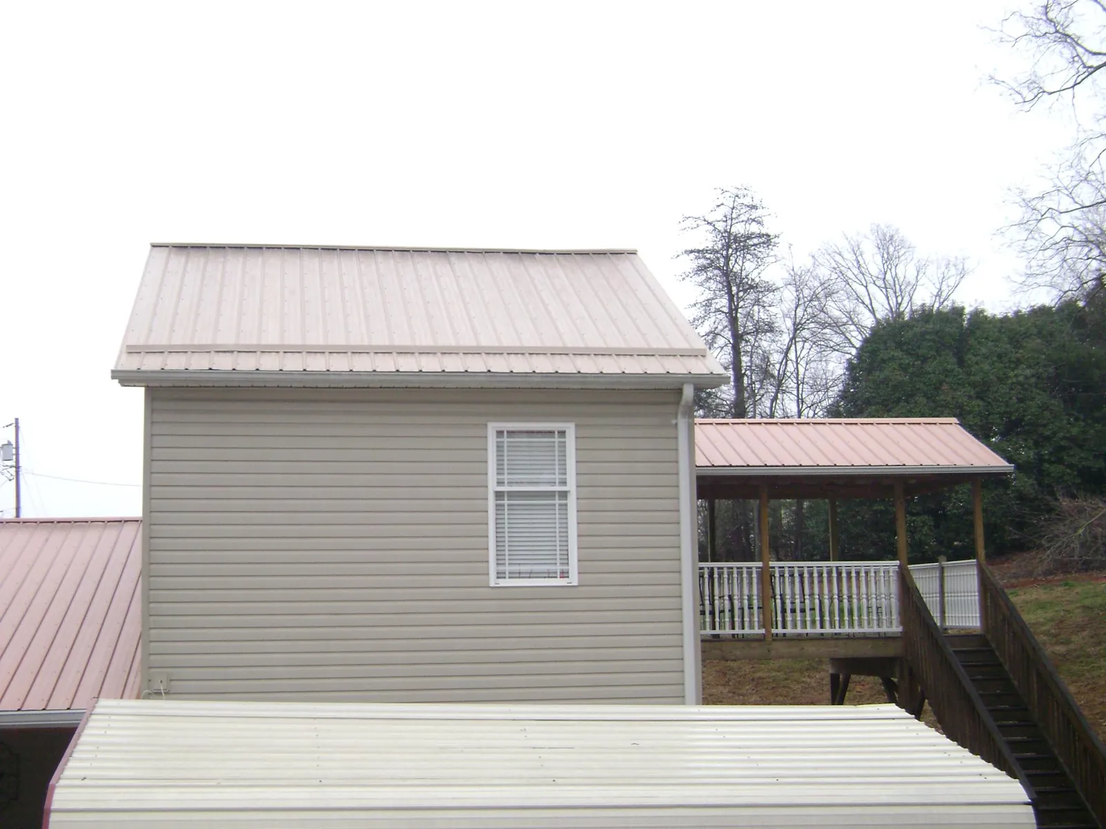 Tan metal roofs on a two story addition and attached porch, from a Roof Replacement job in Scenery Hill